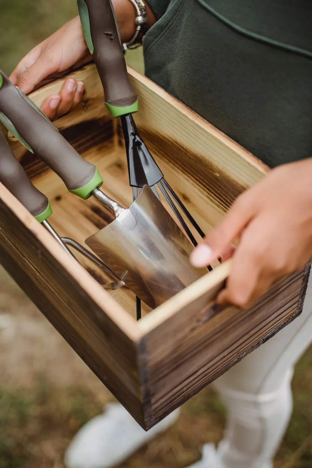 Persona sosteniendo herramientas de jardinería de acero en caja de madera